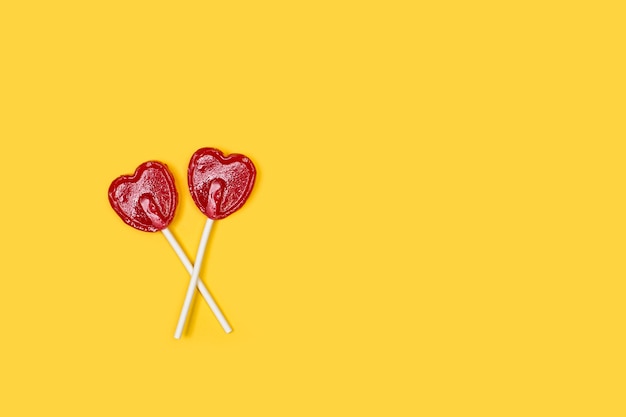 Two red heart shaped lollipops on a yellow background with copy space