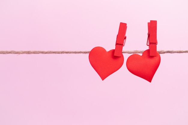 Two red hearts are hung on clips with place for text on a pink background