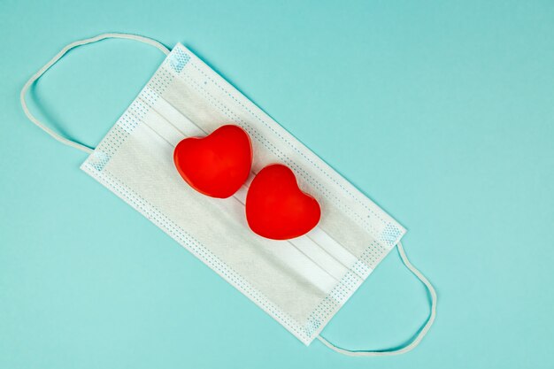 Two red hearts on medical protection mask on light blue surface