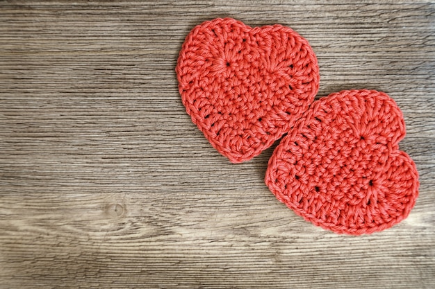 Two red knitted hearts on old natural wood.