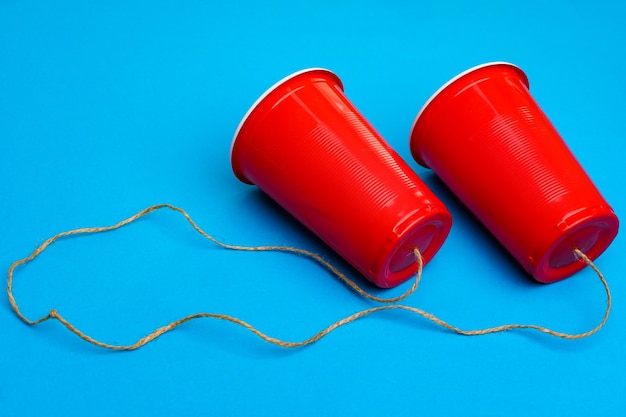 Two red paper cups connected with rope on blue surface toy telephone