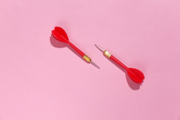 Two red plastic darts with metal tip on pink bright background with deep shadow.