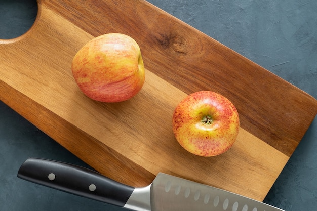 사진 두 개의 빨간색 잘 익은 사과와 큰 요리사의 칼이 도마에 놓여 있습니다.