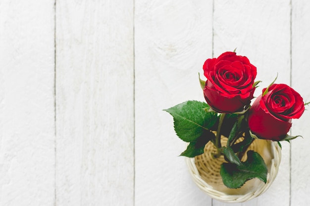 Two red rose in a small basket placed on a white wooden floor.