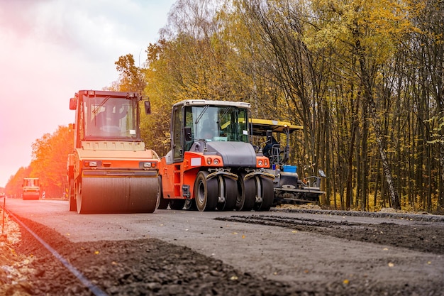 Two red special autos paving new asphalt driving in line one near another. New road construction. Selective focus.