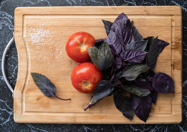 Two red tomatos and purple basil leafs on the wooden board. Top view.