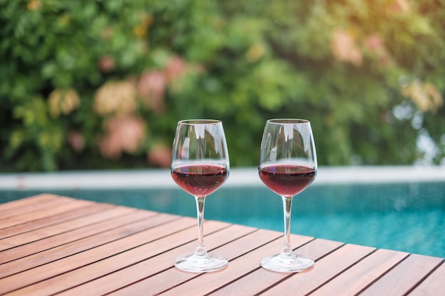 Due bicchieri di vini rossi vicino alla piscina. concetto di viaggio estivo, vacanze, vacanze e buon fine settimana