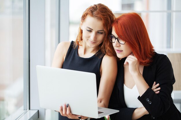 Two redhaired businesswomen in a coworking space with a laptop on the desktop in the office