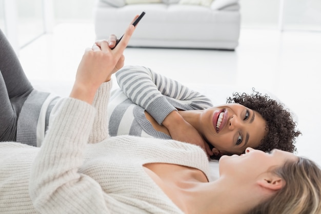 Two relaxed female friends reading text message in bed