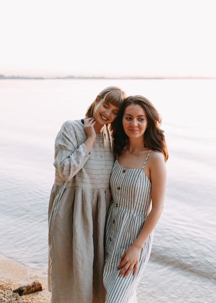 Foto due ragazze rilassate, felici e sorridenti in abiti da sole d'estate vicino al mare.