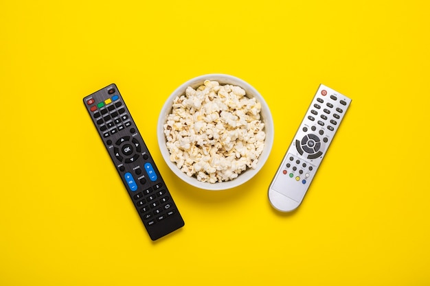 Due telecomandi della tv, sintonizzatore tv e una ciotola di popcorn su giallo