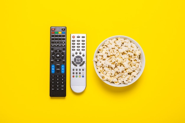 Two remotes from the TV, TV tuner and a bowl of popcorn on yellow