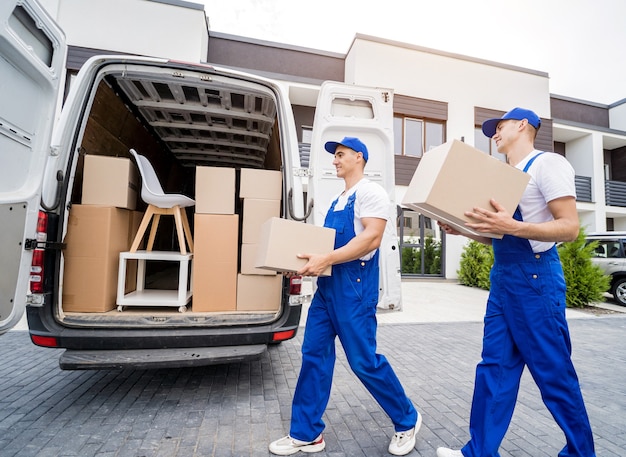 Two removal company workers are loading boxes and furniture into a minibus