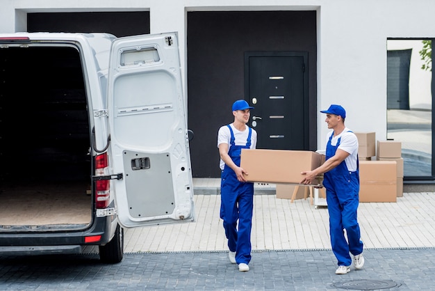 Two removal company workers are loading boxes and furniture into a minibus