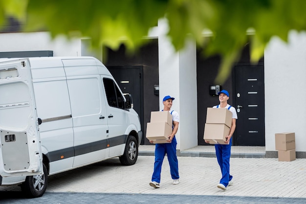 Two removal company workers are loading boxes and furniture\
into a minibus