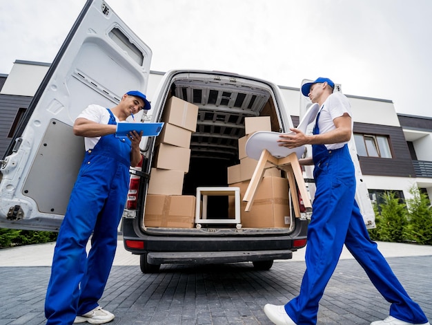 Two removal company workers are loading boxes and furniture into a minibus