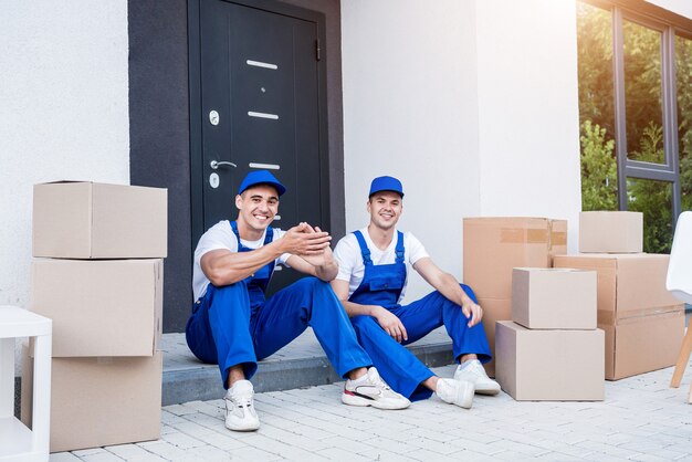 Two removal company workers have a break while sitting on the step