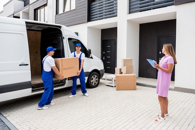 Two removal company workers unloading boxes from minibus into customers home