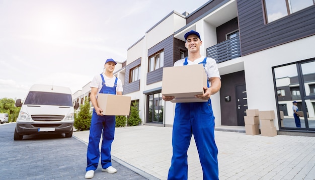 Two removal company workers unloading boxes from minibus into customers home