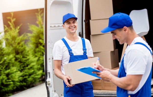 Two removal company workers unloading boxes from minibus into new home