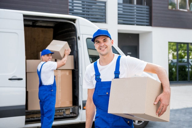 Two removal company workers unloading boxes from minibus into new home