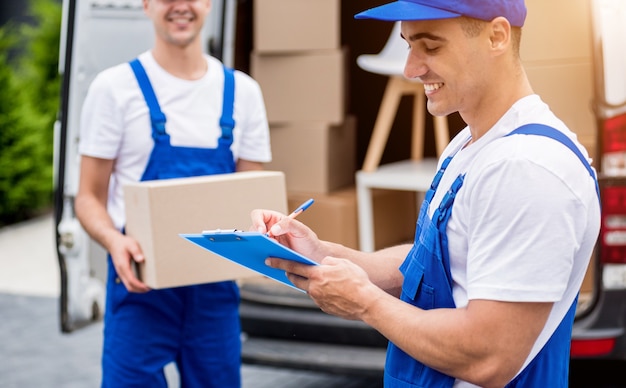 Two removal company workers unloading boxes from minibus into new home