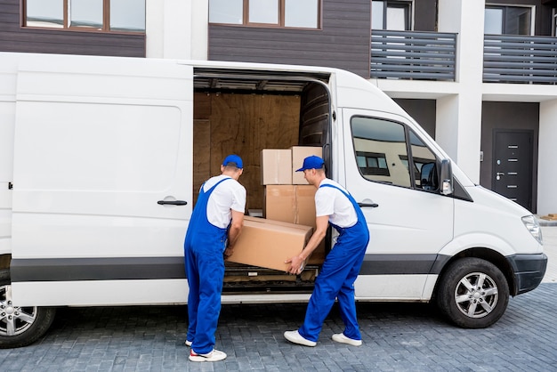 Two removal company workers unloading boxes from minibus into new home