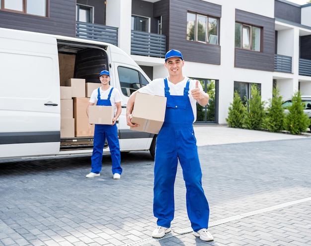 Two removal company workers unloading boxes from minibus into new home