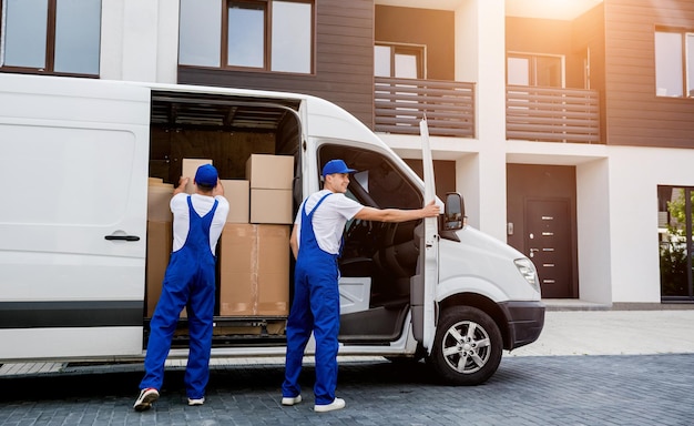 Two removal company workers unloading boxes from minibus into new home