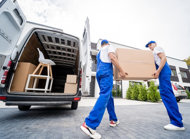 Двое рабочих компании по переезду выгружают ящики и мебель из микроавтобуса