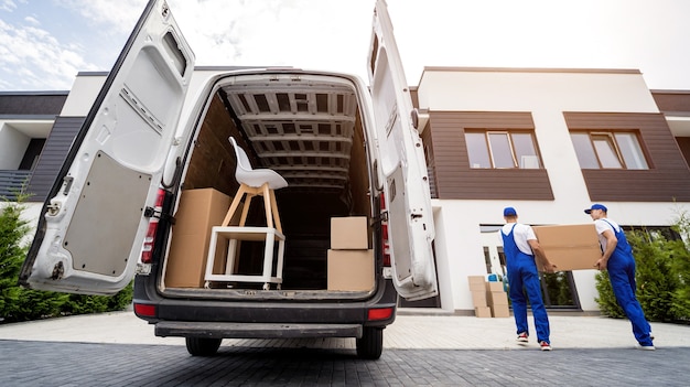 Two removal company workers unloading boxes and furniture from\
minibus