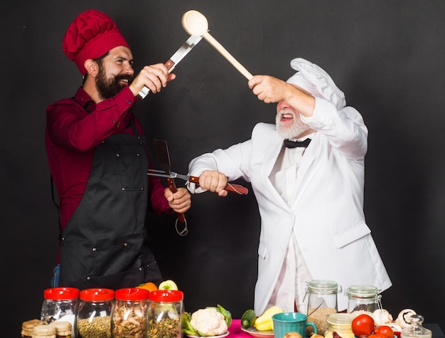 Two restaurant chefs or bakers in uniform fighting in kitchen cooking food competition of chef