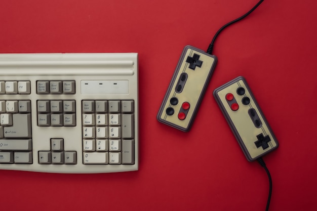 Two retro gamepads and old pc keyboard on red background. Gaming, video game competition. Top view