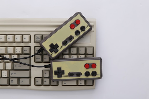 Two retro gamepads and old pc keyboard on white background.\
gaming, video game competition.