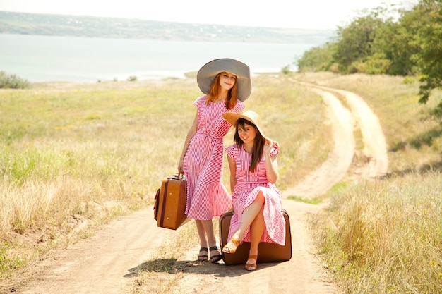 Foto due ragazze in stile retrò con valigie in campagna.