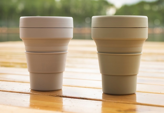 Two reusable eco cups on wooden table in nature. Sustainable lifestyle and zero waste concept.