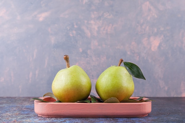 Two ripe green pears with leaves placed on a wooden pink board. 