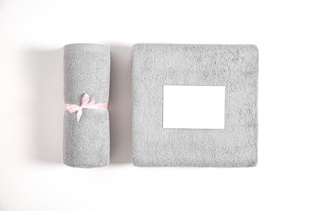 Two rolled and folded terry towels tied by pink ribbon isolated. Stack of grey terry towels with white empty cartoon card against a white background. Top view.