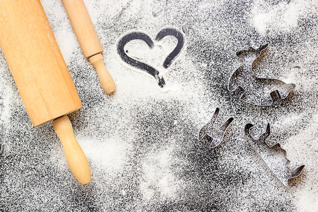 Two rolling pins and cookie cutters are on the table with flour View from above