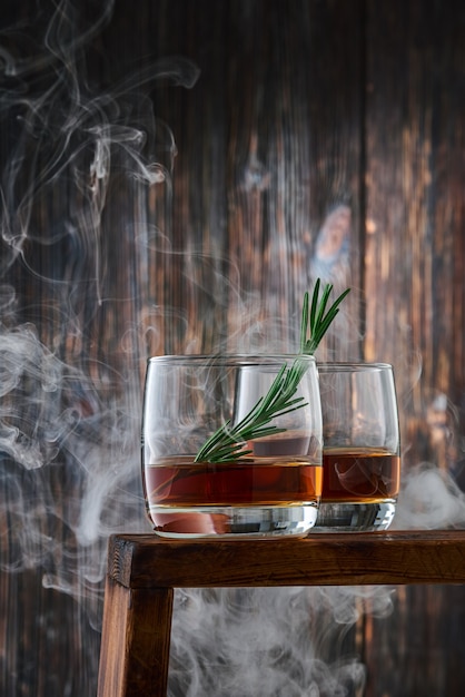 two round glasses with a shot of whiskey and a sprig of rosemary