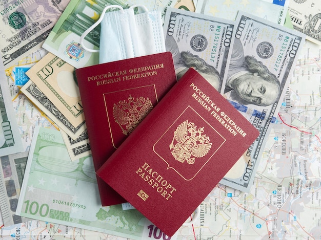 写真 2つのロシアのパスポートがドルとユーロの請求書に記載されていますパスポートの1つに医療用マスクが取り付けられていますパンデミックと病気の間の旅行の概念上面図フラットレイ