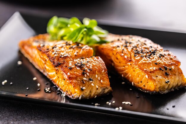 Photo two salmon fillets baked until crispy sprinkled with sesame on a black plate