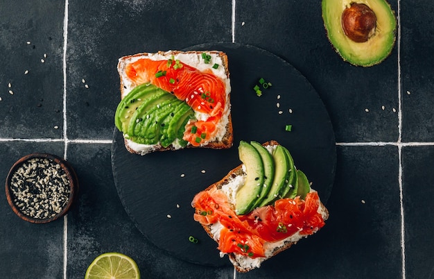 Two salmon toats with cream cheese and avocado slices on black tile background Morning healthy