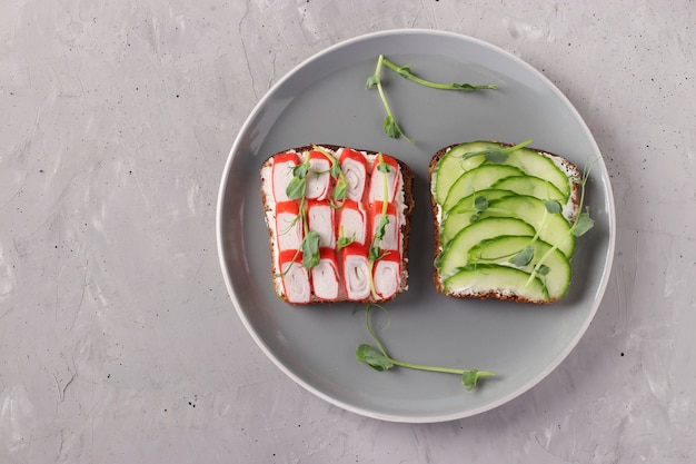 Two sandwiches with cream cheese, cucumbers and crab sticks decorated with microgreens peas