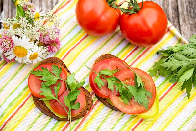 Two sandwiches with herbs and tomatoes on a wooden table.