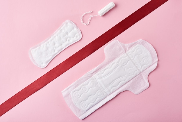 Two sanitary pads and red ribbon on a pink 