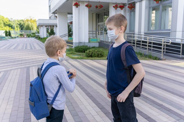 Фото Двое школьников в медицинских масках с рюкзаками в медицинских масках стоят на фоне