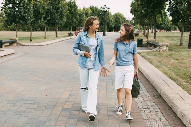 Photo two schoolgirls are holding a tablet in their hands and watching a video laughing on the way