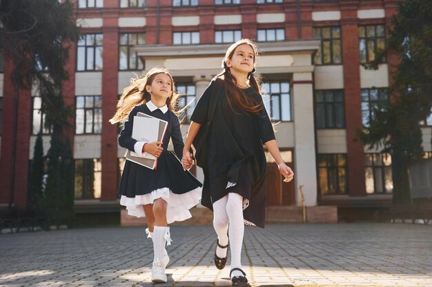 Фото Две школьницы бегают вместе на улице возле здания школы