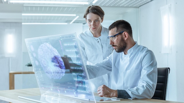 Two scientists in lab coats look at a computer screen with a brain on it.